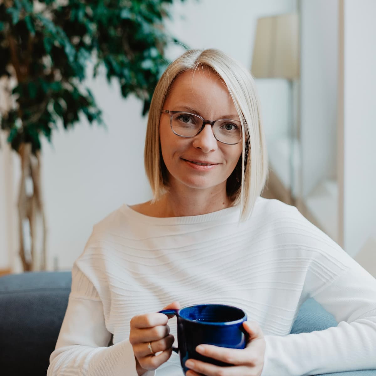 Maria-Kosmala-Bazi-Reading-Coach-Mentorin Maria Kosmala – ruhig und zugewandt mit einer Tasse in der Hand, auf dem Sofa sitzend, bereit für ein vertrauensvolles Gespräch.