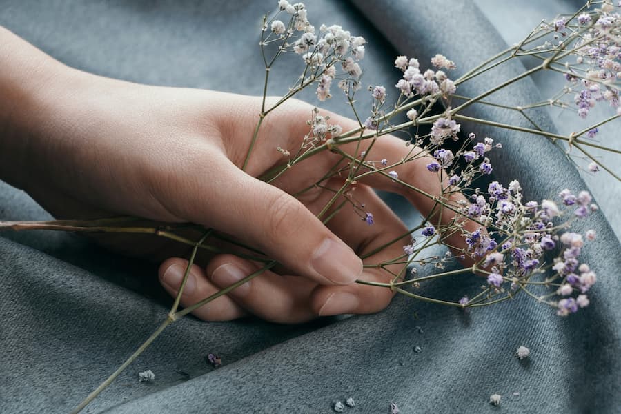 Zarte Frauenhand hält getrocknete Schleierkraut-Blüten auf weichem Stoff – ein Sinnbild für stille Verbundenheit und die Schönheit des Einfachen.