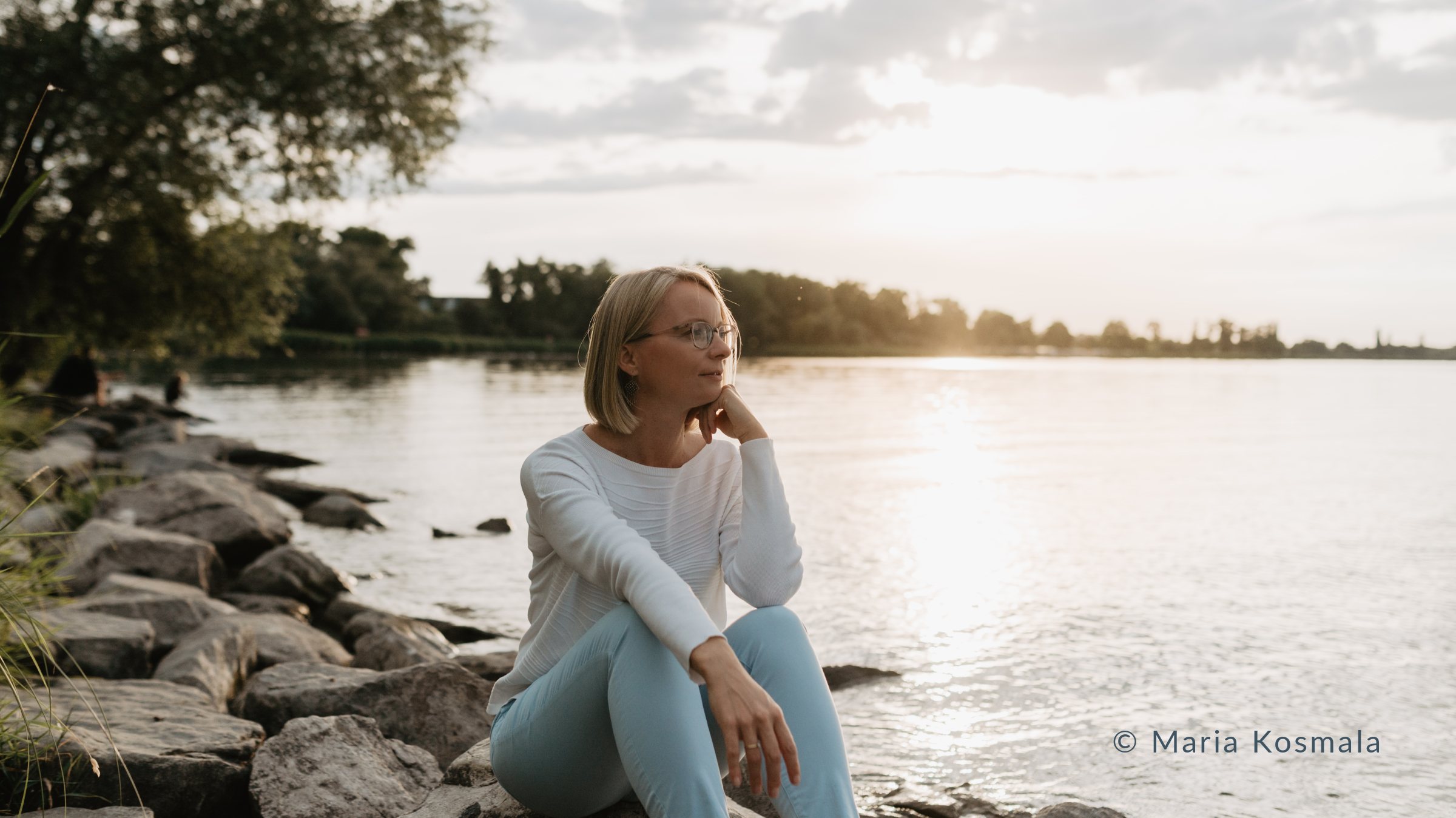 Maria Kosmala sitzt am Ufer des Bodensees im Licht der tief stehenden Abendsonne – Sinnbild für die ruhigere Jahresenergie im Jahr der Feuer-Ziege 2027 in der chinesischen Astrologie Bazi Suanming.